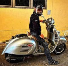 a man sitting on the back of a silver motor scooter in front of a yellow building