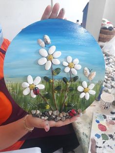 a woman holding up a painted plate with white flowers and ladybugs on it