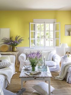 a living room with yellow walls and white furniture in the center, along with flowers on the coffee table