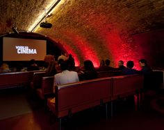 people are sitting in benches and watching a movie on the wall behind them is a brick tunnel with red lights