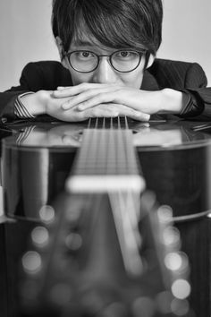 a man with glasses is holding his hands on the neck of a guitar and looking at the camera