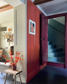 a living room with red walls and white trim on the door, stairs in the background