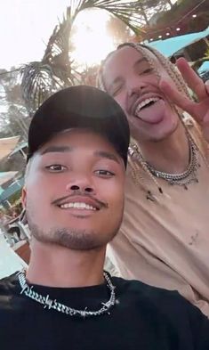 two men are smiling and posing for a selfie in front of a palm tree