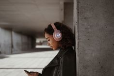 a woman with headphones on looking at her cell phone while leaning against a wall