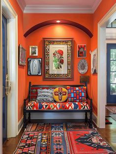 a living room with an orange wall and colorful rugs on the wooden flooring