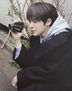 a young man sitting on the ground holding up a camera