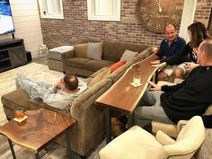 three people sitting on couches in a living room with a large wooden table next to them