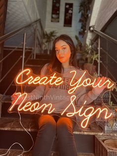 a woman sitting on the steps holding a neon sign that reads create your moon sign