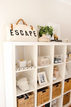 a white bookcase filled with baskets next to a wall mounted sign that reads escape