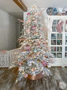 a white christmas tree with pink and silver ornaments on it in a living room next to a china cabinet