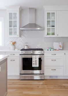 a stove top oven sitting inside of a kitchen next to white cupboards and drawers