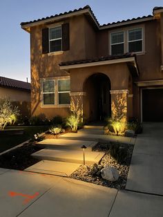 a house that is lit up with lights in the front yard and landscaping around it