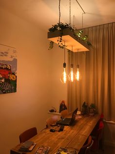 a wooden table topped with a laptop computer next to a plant filled light bulb chandelier