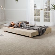 a woman laying on top of a bed in a bedroom next to a plant and window