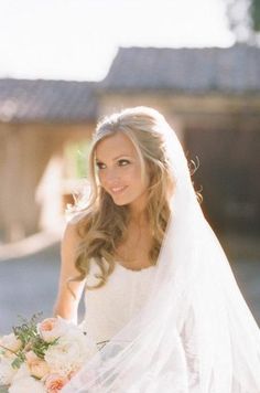 a beautiful young woman holding a bouquet of flowers in her hand while wearing a wedding dress