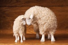 two white sheep standing next to each other on a wooden floor