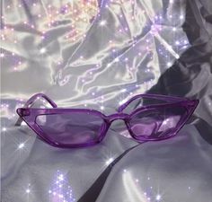 a pair of purple glasses sitting on top of a white sheet covered in sparkling lights