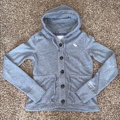 Nwot Abercrombie & Fitch Women’s Medium (8-10) Gray Hooded Full Button Jacket/Sweatshirt. 60% Cotton 40% Polyester. 19” Pit To Pit (Buttoned), 29.5” Sleeve Length With 3” Ribbed Cuffs & 23” Long. 5 Wood Button, Drawstrings & Two Front Pockets With Adjustable Tie Waist. White Embroidery On Left Breast & Sleeve. Nbw. Can Be Worn As A Jacket Or Sweatshirt. Unique Fit & Style. Lightweight With Blue Plaid Accents Inside. Unique Fits, White Embroidery, Jacket Buttons, Dream Clothes, Hooded Jacket, New Outfits, Fitness Fashion, Fashion Inspo Outfits, Winter Outfits