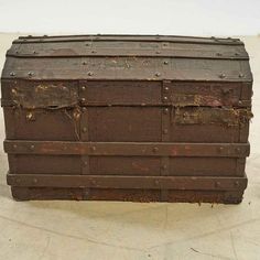 an old trunk sitting on top of a cement floor in front of a white wall