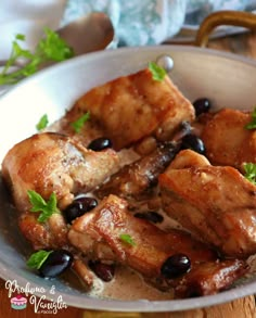 a bowl filled with meat and olives on top of a wooden table