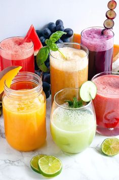 several different types of drinks are lined up on a table with limes, blueberries, and watermelon