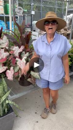 a woman wearing a hat and sunglasses standing in front of potted plants