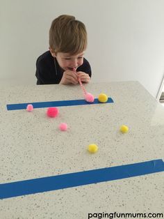 a young boy sitting at a table with some balls in front of him and an article about the pom pom & straw challenge