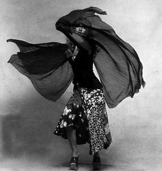 a woman is dancing with her hands in the air while wearing a long skirt and black top