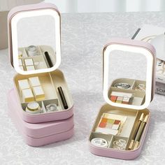 two small pink boxes with makeup and other items in them sitting on a white table