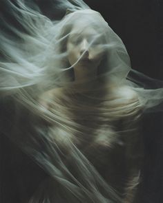 a woman with her hair blowing in the wind while she is wearing a white dress