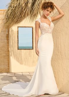 a woman in a white wedding dress standing next to a straw hut on the beach