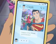 a person holding up a cell phone with an image of superman on the screen and flowers in front of them