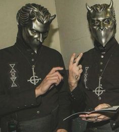 two men dressed in devilish clothing with horns on their heads and hands, one holding an open book