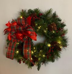 a christmas wreath hanging on the wall with red bows and pineconis around it