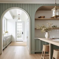 an archway leads into a kitchen with green walls and wood flooring, along with white cabinets