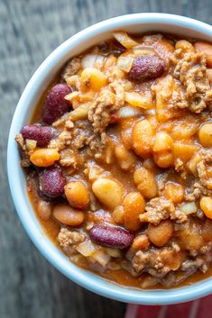 a white bowl filled with chili and beans on top of a wooden table next to a red napkin