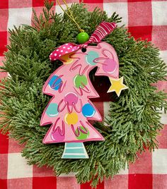 a pink christmas tree ornament sitting on top of a green wreath with red and white checkered tablecloth