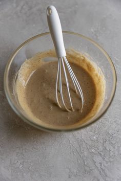 a whisk in a glass bowl filled with brown liquid on top of a table