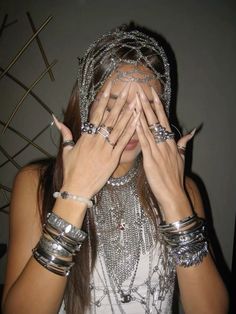 a woman covering her face with silver jewelry