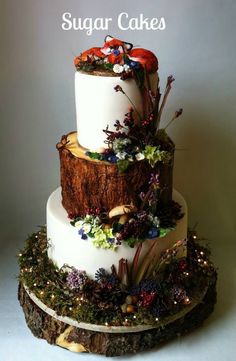 a three tiered cake decorated with flowers and leaves on a tree stump, surrounded by greenery