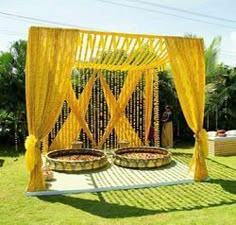 an outdoor ceremony setup with yellow drapes and flower baskets on the ground, surrounded by greenery