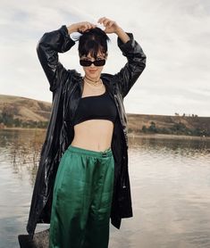 a woman standing in front of a body of water with her hands on her head