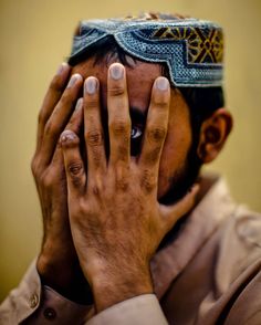 a man covering his face with his hands while wearing a headdress on top of his head