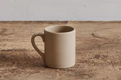 a white cup sitting on top of a wooden table next to a wall and floor