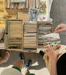 two people sitting at a table with many books and papers in front of them on the floor