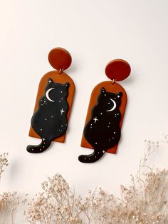 two black cats with crescent moon and stars on them are hanging from orange acrylic earrings