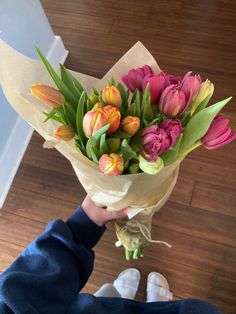 a person holding a bouquet of tulips on top of a hard wood floor