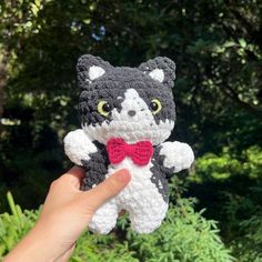 a hand holding a small crocheted cat with a red bow tie on it