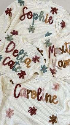 three sweaters with words written on them, one is white and the other has multicolored flowers