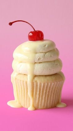 a cupcake with white frosting and a cherry on top is sitting on a pink surface